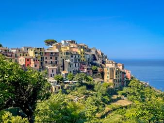 Colorful houses of Corniglia perched on a cliff in Cinque Terre, surrounded by lush green vegetation with the blue Mediterranean Sea in the background.