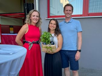 Drei lächelnde Personen beim Eurofun Touristik Sommerfest. Frau in rotem Kleid und Mann in blauem Polo neben Frau mit Geschenkkorb und Pflanze.