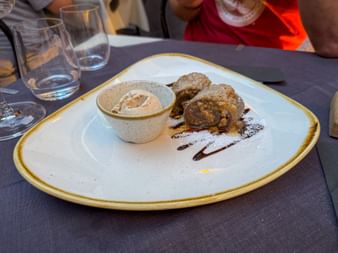 White plate with pastries, ice cream in a ceramic bowl, and chocolate sauce decoration on a restaurant table with water glasses.