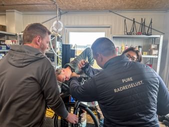 Group of people in a bike workshop during Eurofun Touristik Training Days 2026. A person with 'PURE RADREISELUST' jacket works on a bicycle.