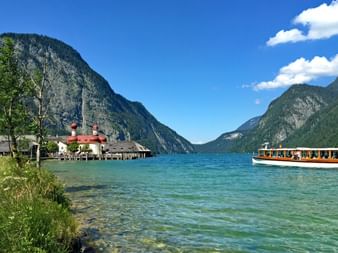Königssee lake with St. Bartholomä church featuring red onion domes on the shore, surrounded by steep mountains and clear turquoise water.