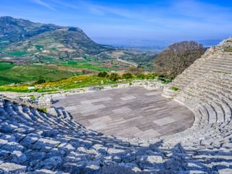 Blick vom Theater Segesta Antikes griechisches Theater in Segesta mit Steinreihen mit Blick auf sizilianische Landschaft mit grünen Feldern und Bergen unter blauem Himmel.