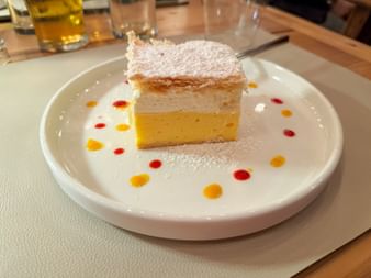Slice of Bled cream cake with layers of puff pastry, vanilla custard, and whipped cream, dusted with powdered sugar on a white plate.