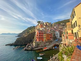 Bunte Häuser des Dorfes Riomaggiore auf Klippen über dem Mittelmeer in Cinque Terre, mit Booten in einem kleinen Hafen.