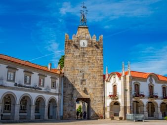 Torre do Relógio, a medieval stone clock tower with crenellations in Caminha, Portugal, flanked by white buildings with orange roofs.