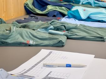 Colorful t-shirts and clothing items spread on a table with a document and pen in the foreground at Eurofun Touristik Training Days 2026.