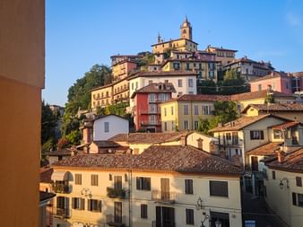Colorful hillside village of Monforte in Piedmont with multi-story buildings in warm tones and a church with bell tower at the summit.