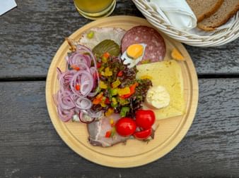 Wooden platter with cold cuts, cheese, pickles, onions, tomatoes, and bread basket on rustic table at Lindlingalm in Saalbach-Hinterglemm.