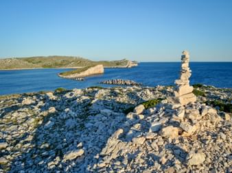 Steinpyramide auf felsiger Küste im Kornati-Nationalpark, Norddalmatien. Blaues Adriatisches Meer mit kleinen Inseln im Hintergrund.