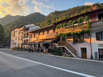 Traditionelles Restaurant mit Holzbalkonen und Außenterrasse in Kobarid, Julische Alpen. Bewaldete Berge erheben sich im Hintergrund unter Abendhimmel.