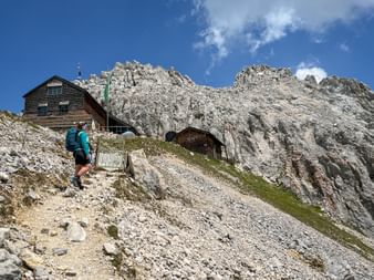 Wanderer mit türkisfarbenem Rucksack auf felsigem Bergpfad zur Meilerhütte im Wettersteingebirge mit dramatischen Kalksteinfelsen.