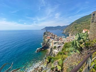 Dorf Manarola auf felsigen Klippen über dem türkisfarbenen Ligurischen Meer, mit bunten Häusern und grünen Hängen unter blauem Himmel.