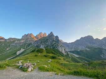 Morgenansicht der zerklüfteten Dachstein-Gipfel mit grünen Almwiesen im Vordergrund. Felsige Bergformationen leuchten im frühen Sonnenlicht.
