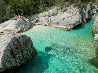 Kristallklarer türkiser Soča-Fluss fließt durch weiße Kalksteinfelsen. Menschen ruhen auf glatten Felsen über dem Wasser in den Julischen Alpen.