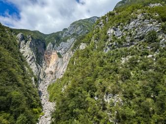 Boka-Wasserfall, der steile Felsklippen in den Julischen Alpen hinabstürzt, umgeben von dichtem grünem Wald und Kalksteinformationen.