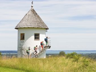 Gruppe von Wanderern auf der Treppe eines weißen runden Wasserturms mit Kegeldach in Bergham bei Bernau, mit Bergseeblick im Hintergrund.