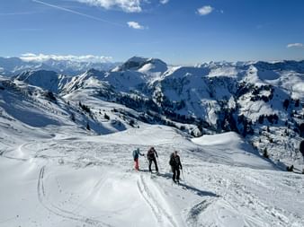 Drei Skitourengeher auf verschneitem Hang mit Panoramablick auf schneebedeckte Alpengipfel in Maria Alm-Dienten unter blauem Himmel.