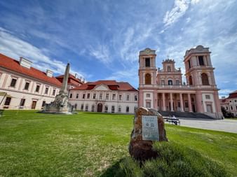 Stift Göttweig Klosteranlage in der Wachau mit rosa Barockkirche, weißen Gebäuden mit roten Dächern, grüner Wiese und blauem Himmel.