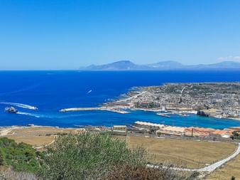 Blick übers Meer von der Stadt Favignana Luftaufnahme der Insel Favignana mit Hafenstadt, türkisfarbenem Wasser und fernen Bergen. Eine Fähre überquert das blaue Mittelmeer.