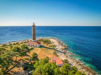 Luftaufnahme des Leuchtturms Veli Rat auf der Halbinsel Dugi Otok mit weißen Gebäuden, felsiger Küste und türkisfarbenem Adriatischem Meer.