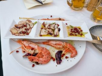 Meeresfrüchtegericht mit gegrillten Garnelen und drei Portionen Oktopus, garniert mit Granatapfelkernen und Olivenöl auf weißen Tellern in Kobarid.