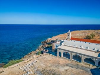 Kloster Apostolos Andreas mit weißen Gebäuden und Glockenturm an felsiger Küste mit Blick auf das blaue Mittelmeer in Zypern.