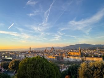 Panoramablick auf Florenz bei Sonnenuntergang mit Dom, Palazzo Vecchio und Arno-Brücken vor Bergkulisse.