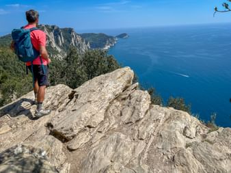Hiker with backpack standing on rocky cliff overlooking the blue Mediterranean Sea near Porto Venere on the Ligurian Coast.