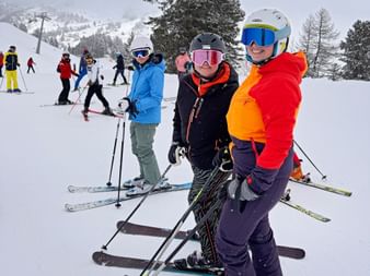 Group of skiers on snowy slope in Obertauern. Three women in foreground wear colorful ski jackets and helmets with goggles.