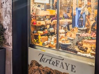 Shop window of TartuFaye displaying various truffle products, cheeses, and gourmet items on wooden shelves in Piedmont-Liguria region.