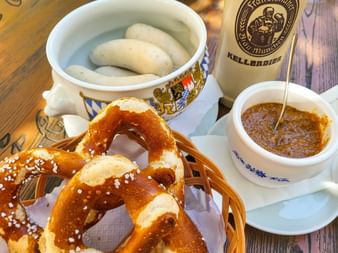 Traditionelles bayerisches Frühstück mit Weißwürsten in einer Schale, einer großen Brezel mit Salz, süßem Senf und einer Kellerbier-Flasche.