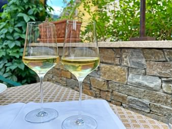 Zwei Gläser Weißwein auf einem Tisch mit Steinmauer und Grün im Hintergrund, Wachau Weinregion zwischen Dürnstein und Weißenkirchen.