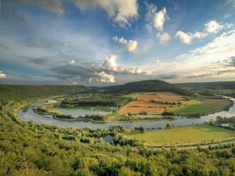 Aerial view of Altmühltal valley with a winding river meander surrounded by green forests, agricultural fields, and hills under a blue sky.
