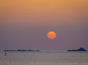 Orange Sonne über ruhigem Meer mit Silhouetten der Kanalinseln am Horizont. Himmel wechselt von Orange zu Violett.