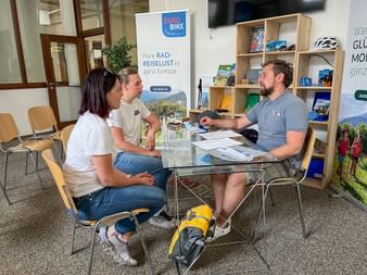 Zwei Kundinnen im Beratungsgespräch mit einem Eurobike-Mitarbeiter an einem Glastisch. Broschüren und ein Banner sind im Büro sichtbar.