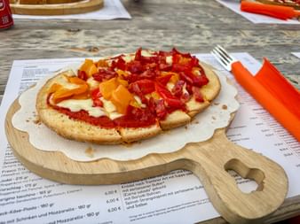Toasted bruschetta topped with red sauce, white cheese, yellow and red bell peppers on a wooden serving board with orange napkin and fork.