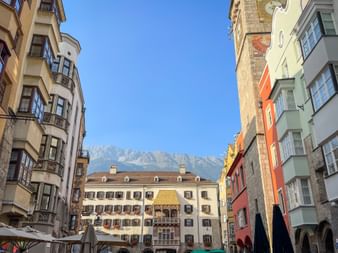 Historic building with golden roof in Innsbruck's old town, surrounded by colorful facades and snow-capped mountains in the background.