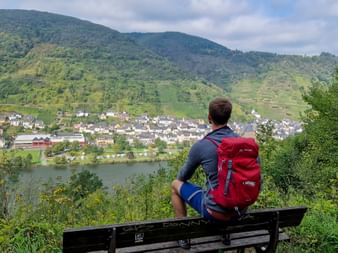 Wanderer sitzt auf Bank mit Blick auf Dorf an der Mosel