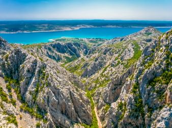 Tiefe Felsenschlucht im Paklenica-Nationalpark mit steilen Kalksteinklippen und grüner Vegetation, mit Blick auf die türkisfarbene Adria.