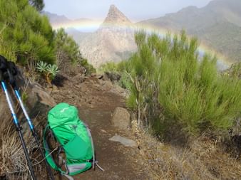 Wanderrucksack und Wanderstöcke, im Hintergrund ein Regenbogen