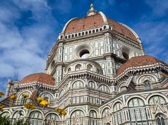 Die ikonische Terrakotta-Kuppel der Kathedrale von Florenz mit weißer Marmorfassade und geometrischen Mustern, von unten gegen blauen Himmel fotografiert.