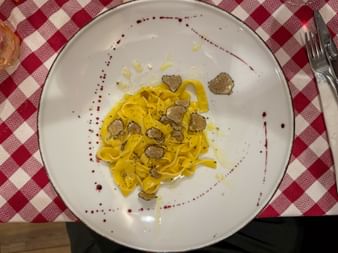 Teller mit gelben Tagliolini-Nudeln mit schwarzen Trüffelscheiben auf einem weißen Teller mit roten Punkten, serviert auf rot karierter Tischdecke.