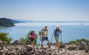 Drei Wanderer mit Rucksäcken und Wanderstöcken stehen auf felsigem Gelände mit Blick auf die Adria bei Triest in den Julischen Alpen.