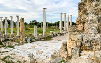 Antike archäologische Stätte von Salamis auf Zypern mit weißen Marmorsäulen, Steinruinen und gepflasterten Böden unter bewölktem Himmel.