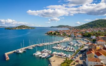 Aerial view of Preko marina on Ugljan Island with sailboats, red-roofed houses, and green hills along the Adriatic coast in North Dalmatia.