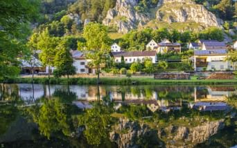 Bayerisches Dorf mit weißen Häusern am Main-Donau-Kanal im Altmühltal, vor dramatischen Kalksteinfelsen und Wäldern.