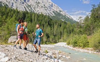 Drei Wanderer mit Rucksäcken und Wanderstöcken stehen an der türkisfarbenen Leutascher Ache in der Zugspitzregion vor Kalksteinfelsen.