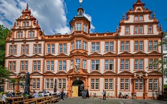 Baroque facade of the Gutenberg Museum in Mainz with ornate orange-white architecture, stepped gables, and central tower under blue sky.