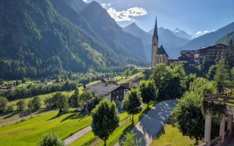 Heiligenblut Dorf mit hochspitziger Kirche umgeben von grünen Wiesen und traditionellen Häusern in einem Alpental mit bewaldeten Bergen.