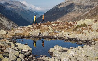 Reflection of two hikers in a mountain lake with panorama